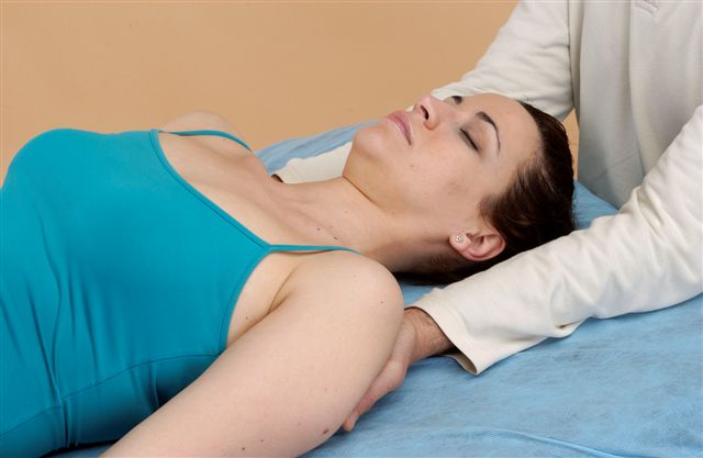 Terapeuta en sesión de Terapia Biodinámica Craneosacral colocando sus manos sobre los hombros de una mujer.